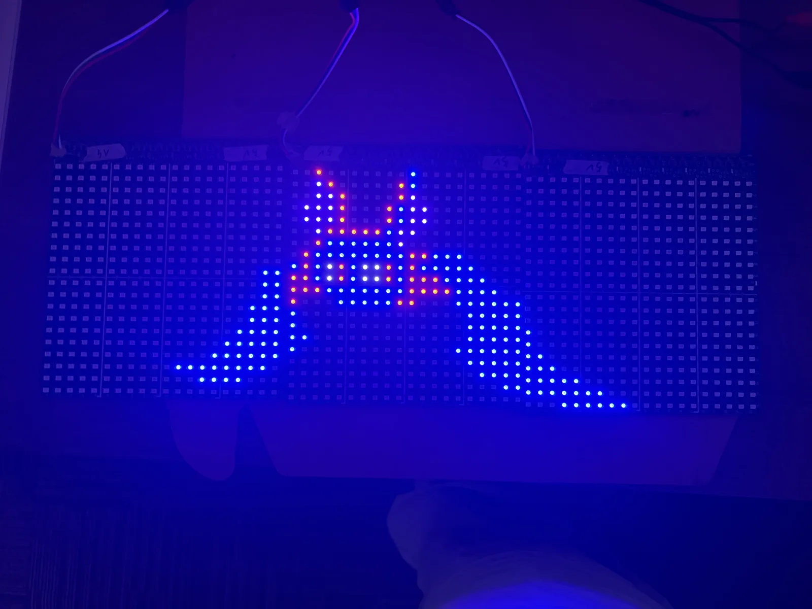 The chained panels lit in a dark room, showing a single pixel graphic in blue, orange and white that runs continuously across the seams between panels.