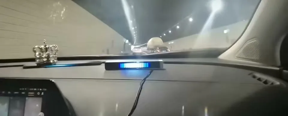 A sound-activated LED bar on a car dashboard lit blue and white, seen from the driver's seat while driving through a lit tunnel.